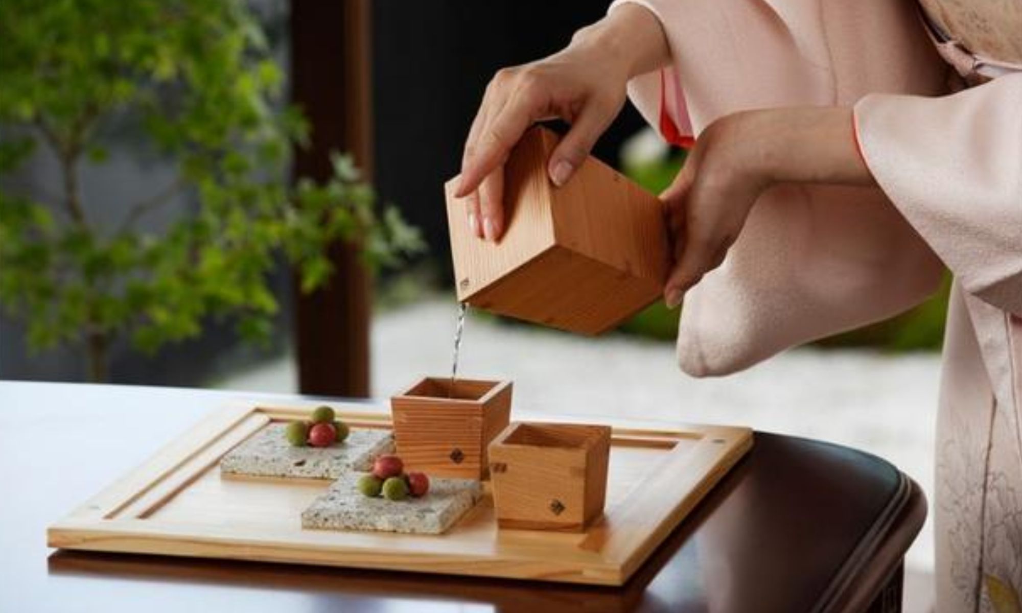 Sake being poured into small wooden masu cups on a tray
